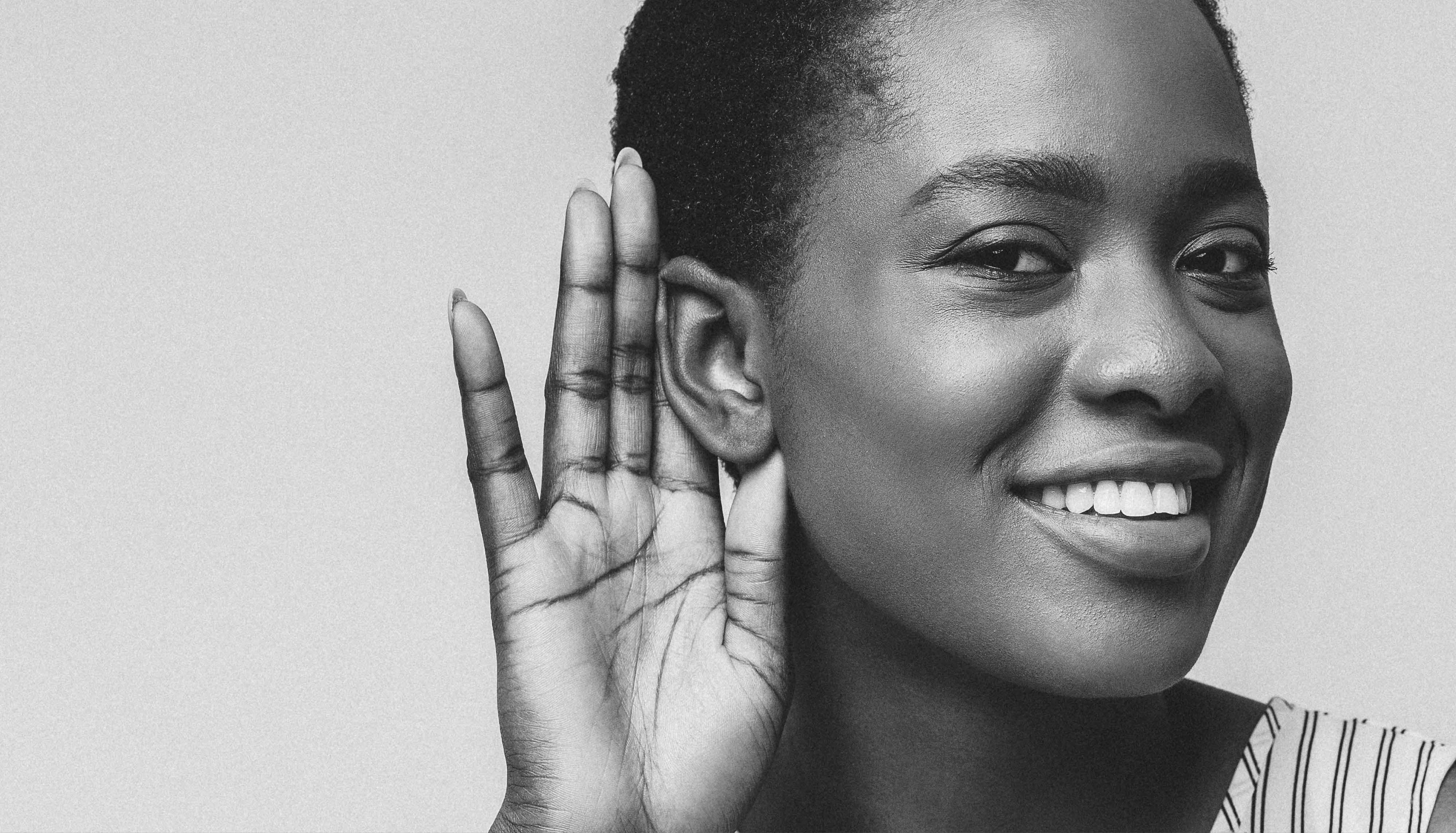 Curious interested african american woman holding hand near ear and trying to hear information, yellow studio background
